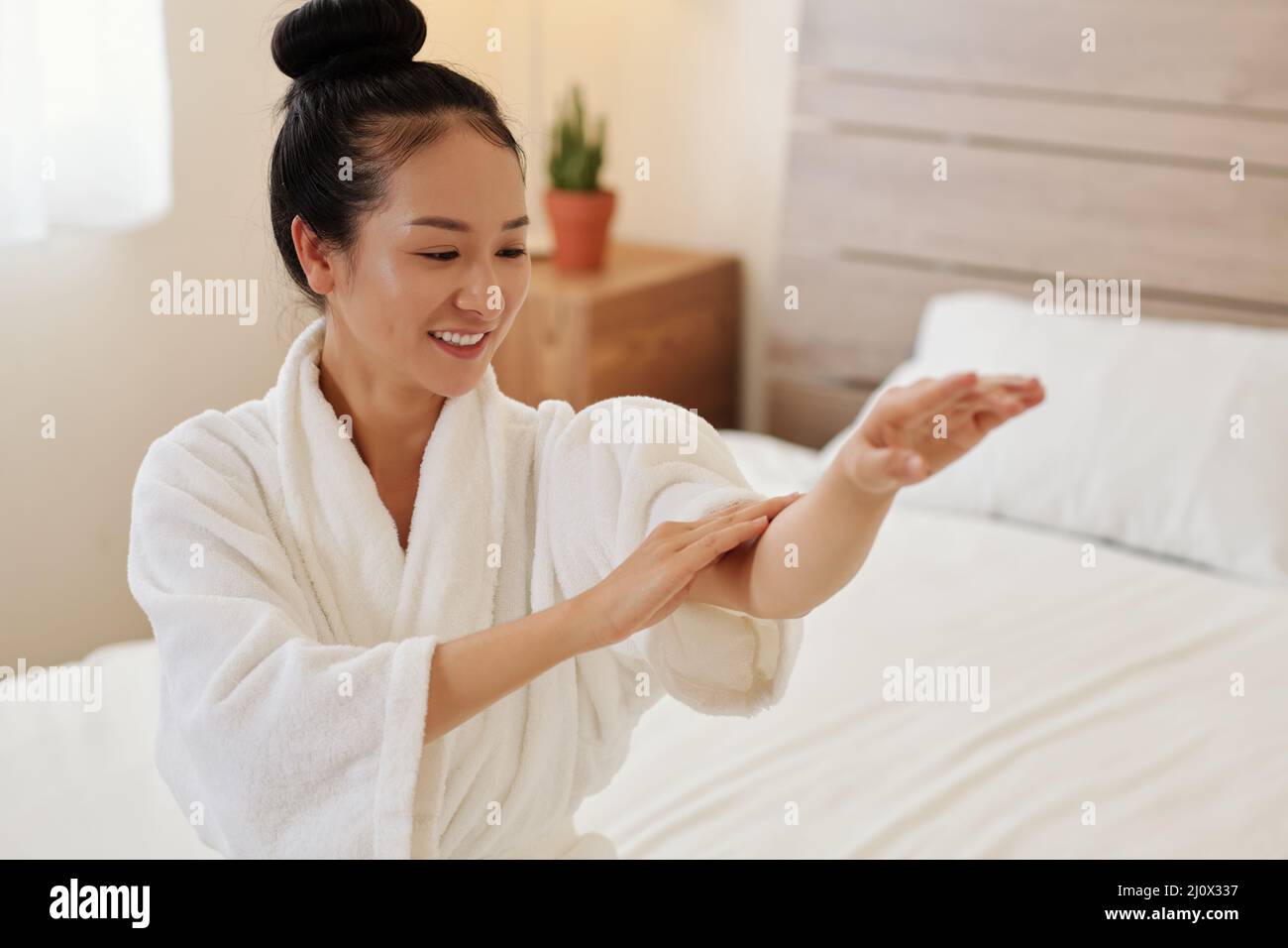 Happly young Asian woman applying body oil on her arms after taking ...