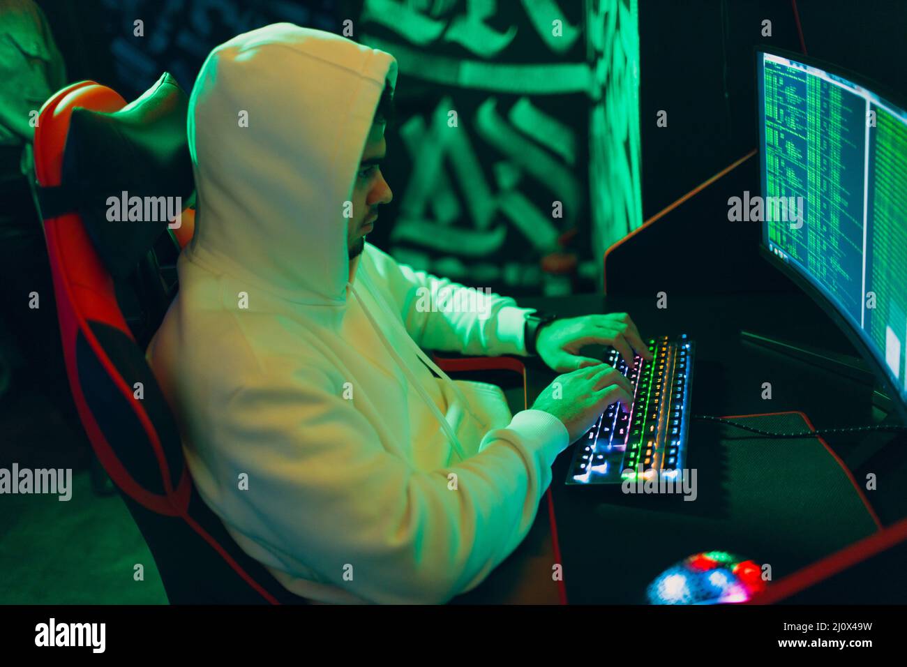 Hacker in hoodie working hacks code site on personal computer with green light Stock Photo