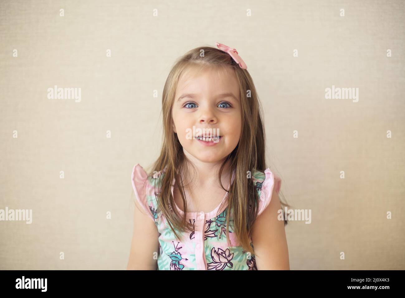 Close up of cute adorable smiling little girl with blue eyes against beige wall indoors Stock Photo