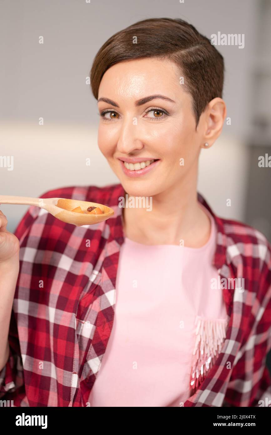 Close up housewife in red plaid shirt and short hair cooking soup on modern kitchen. Smiling woman testing her dish. Chef woman Stock Photo