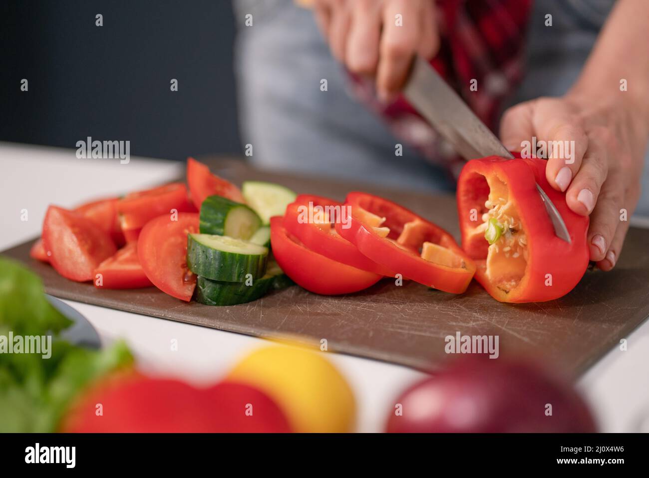 Woman cutting sweet pepper or bell pepper using knife on plastic cut board. Freshly cut vegetables for fresh salad. Healthy leav Stock Photo