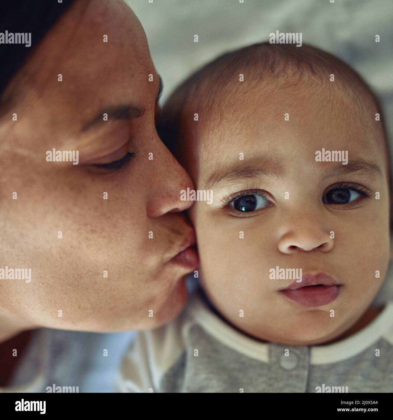 Mothers love their kids instinctively. Shot of a mother kissing her adorable baby boy on the cheek at home. Stock Photo