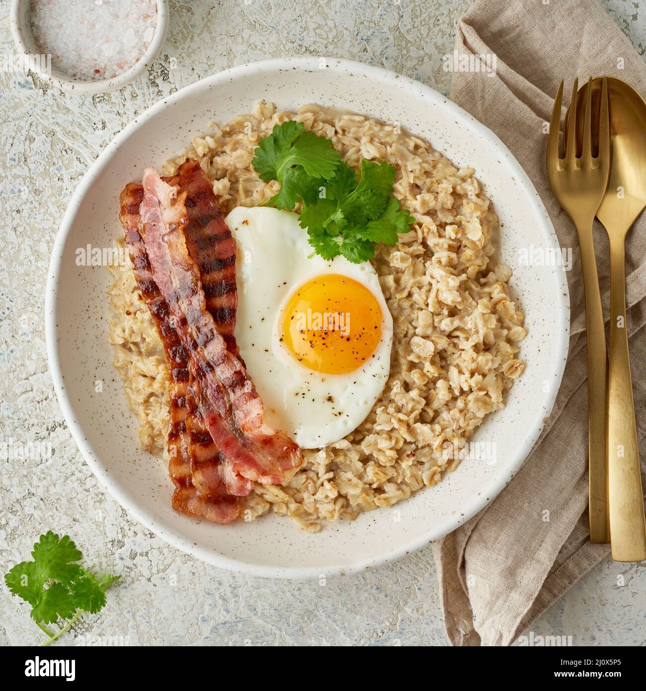 Oatmeal, fried egg, fried bacon. Hearty fat high-calorie breakfast, top view Stock Photo