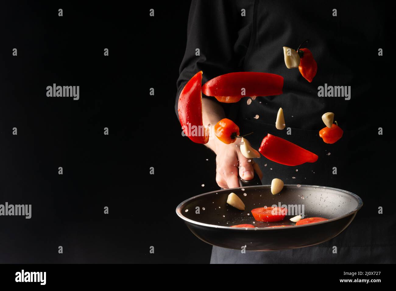 Chef prepares vegetables, roasting on a griddle on a black background, horizontal photo, menu, recipe book, restaurants, healthy and tasty food Stock Photo