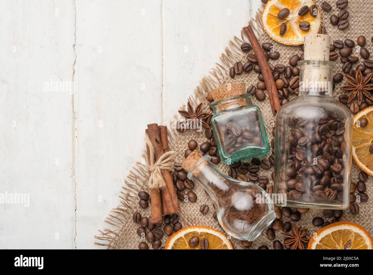 Grains of coffee in a glass jar, with cinnamon, dried oranges, on a light wooden texture. With