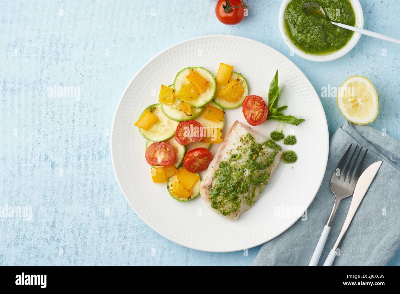 Keto dinner with white fish. Oven baked fillet of cod, pike perch with vegetables and pesto sauce Stock Photo