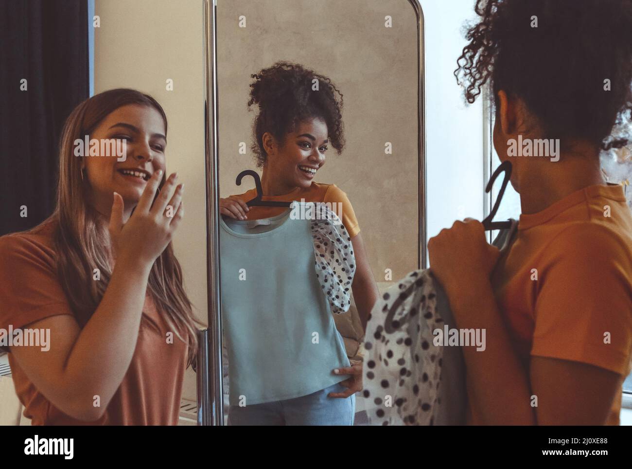 Two young ladies having fun trying on clothes in front of mirror at home Stock Photo