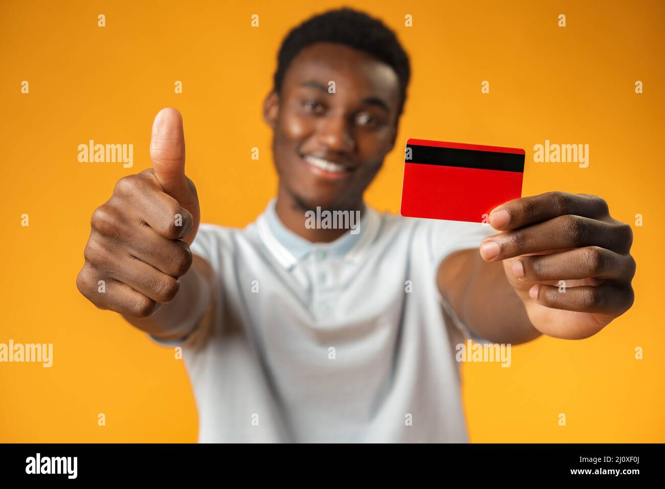 Afro american man holding red credit card against yellow background in ...