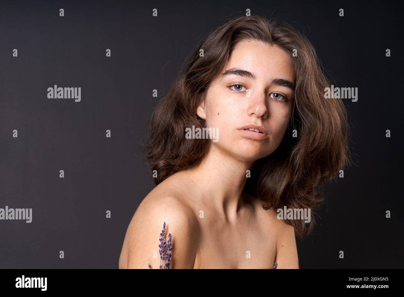 Unshaven armpit concept. Girl is holding lavender flowers in front her armpits. Symbol of unshaven body parts. Body positivity and naturalness. Problems home depilation on black background Stock Photo
