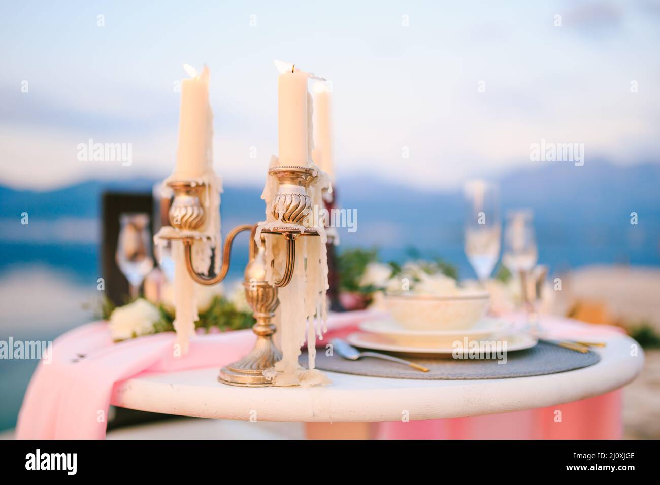 Close-up of a wedding dinner table at reception. Burning candles in a candelabrum on a table with pink cloth and cream plates on Stock Photo