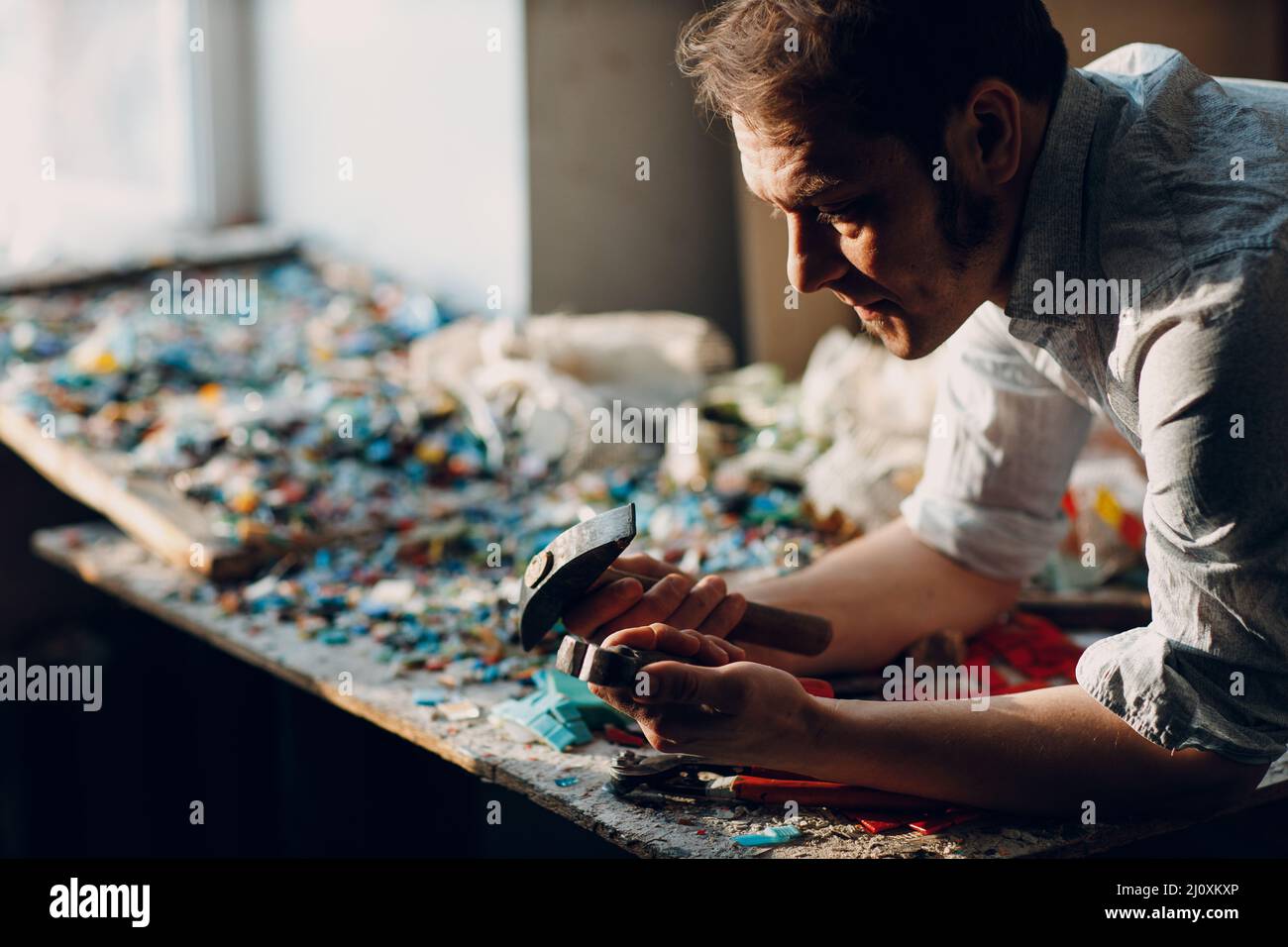Craftsman male master portrait hold hammer and smalt glass pieces in arm hand for mosaic artwork in workshop Stock Photo