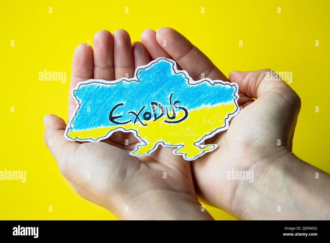 woman's hands hold the map of ukraine painted in the colors of its flag with the word exodus written on it representing the massive flight of the civi Stock Photo