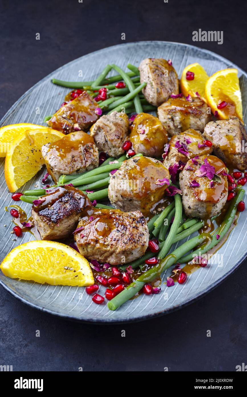 Jusy seared pork pigllet tenderloin fillet meat medallions with orange relish sauce and pomegranate and green baby beans  vegeta Stock Photo