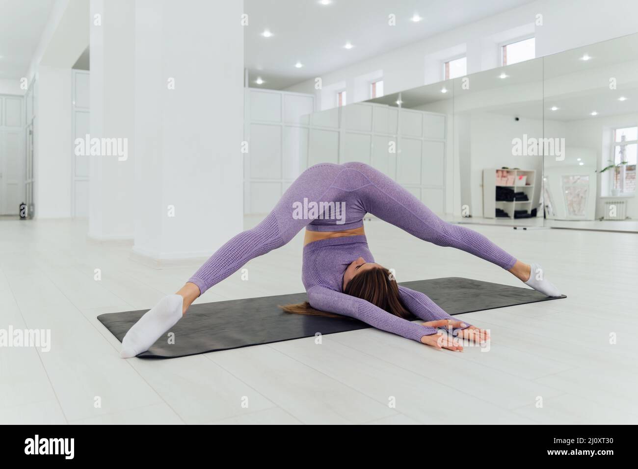 Woman in trendy colour sportswear doing stretch and split in gym Stock Photo