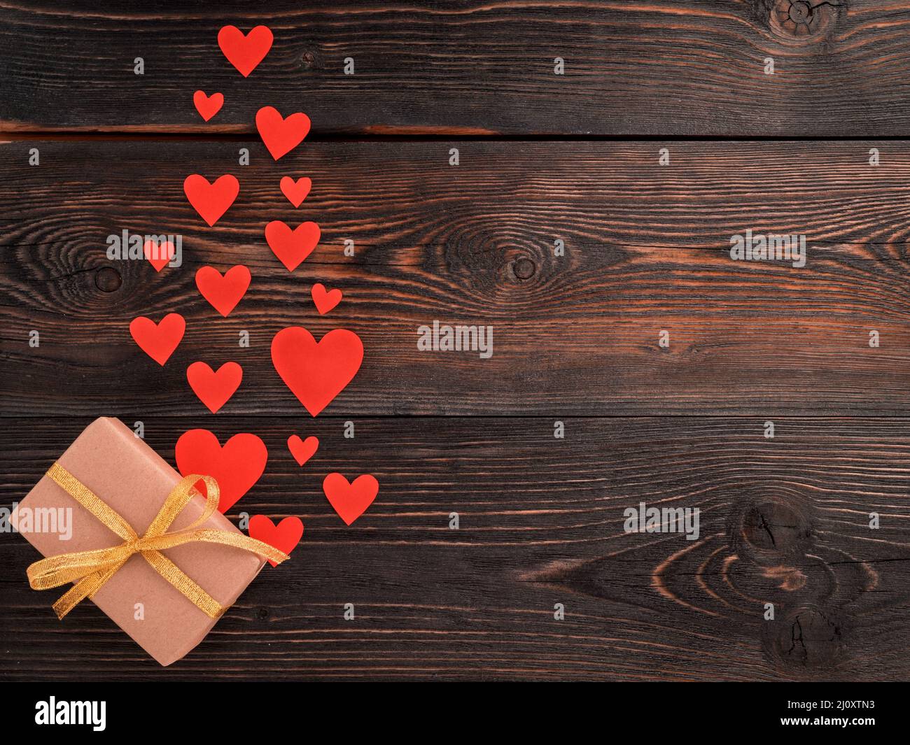 Gift box with ribbon and lots of little red hearts on wooden texture dark background, top view Stock Photo