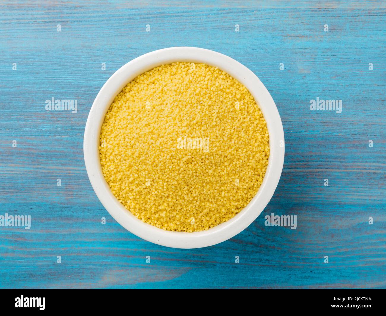 White bowl with raw couscous on blue wooden background, top view. Traditional Moroccan food Stock Photo