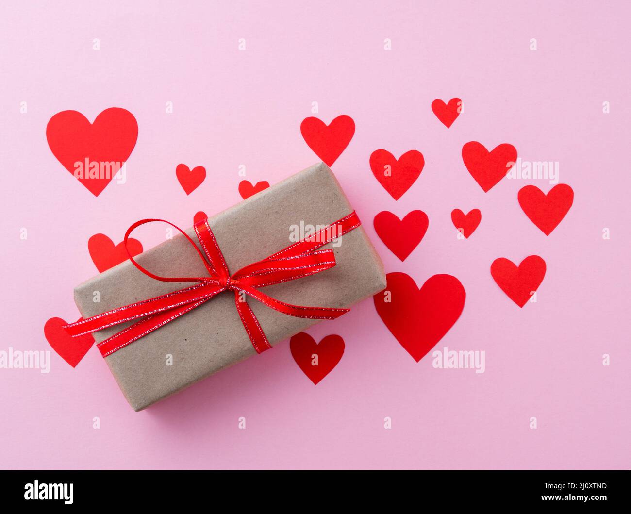 Gift box in kraft brown paper with a red ribbon on a pink background with lots of red hearts, top view Stock Photo