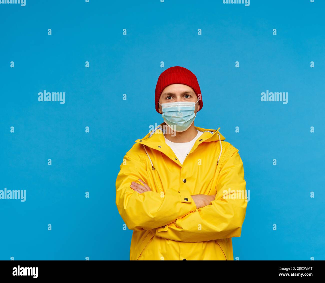 Waisted portrait of man in protective medical mask stands with arms crossed and looks at camera Stock Photo
