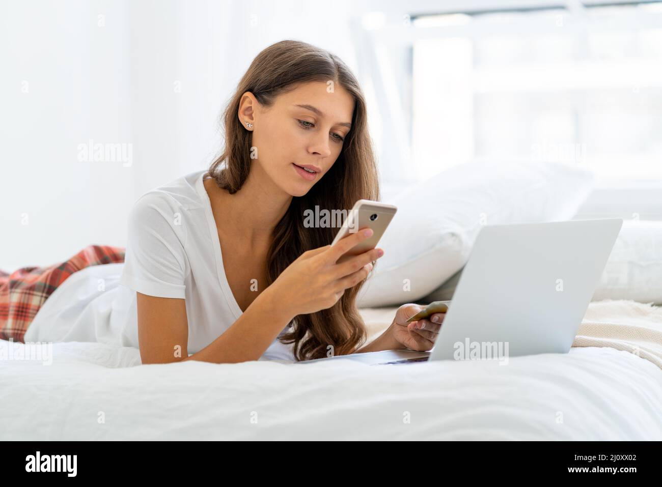 Young woman shopping online, entering code from SMS message on mobile phone, security Stock Photo