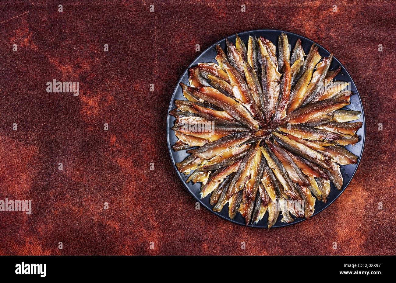 European anchovy fish fillet in a black plate on a red brown leather background top view Stock Photo