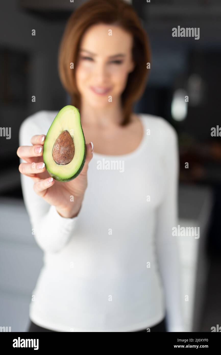 Young Caucasian woman holding halved avocado depth of field, vertical Stock Photo