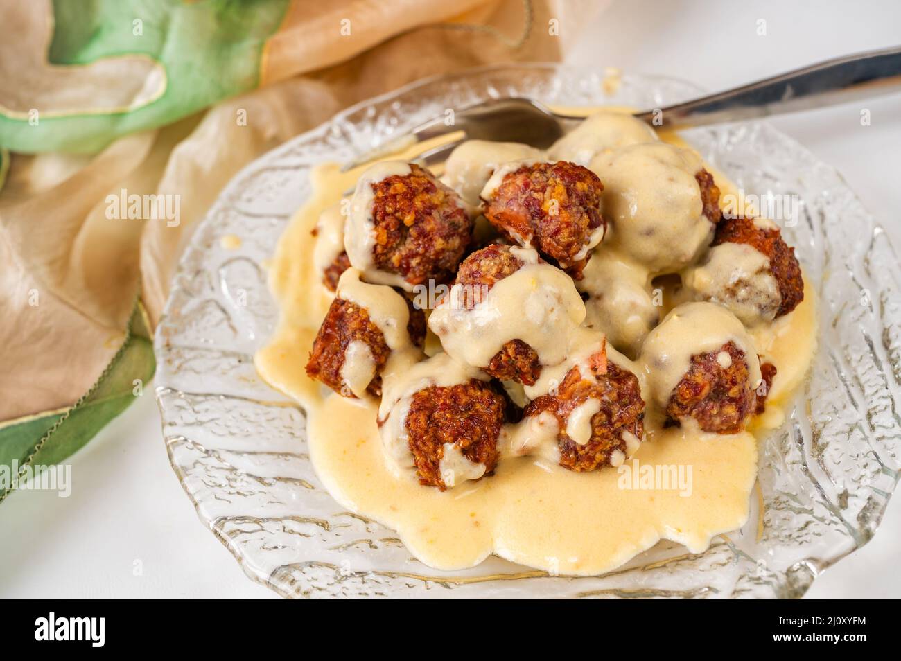Fried meat ball with cheese and lemon sauce on glass plate, fork and green scarf, closeup. Stock Photo