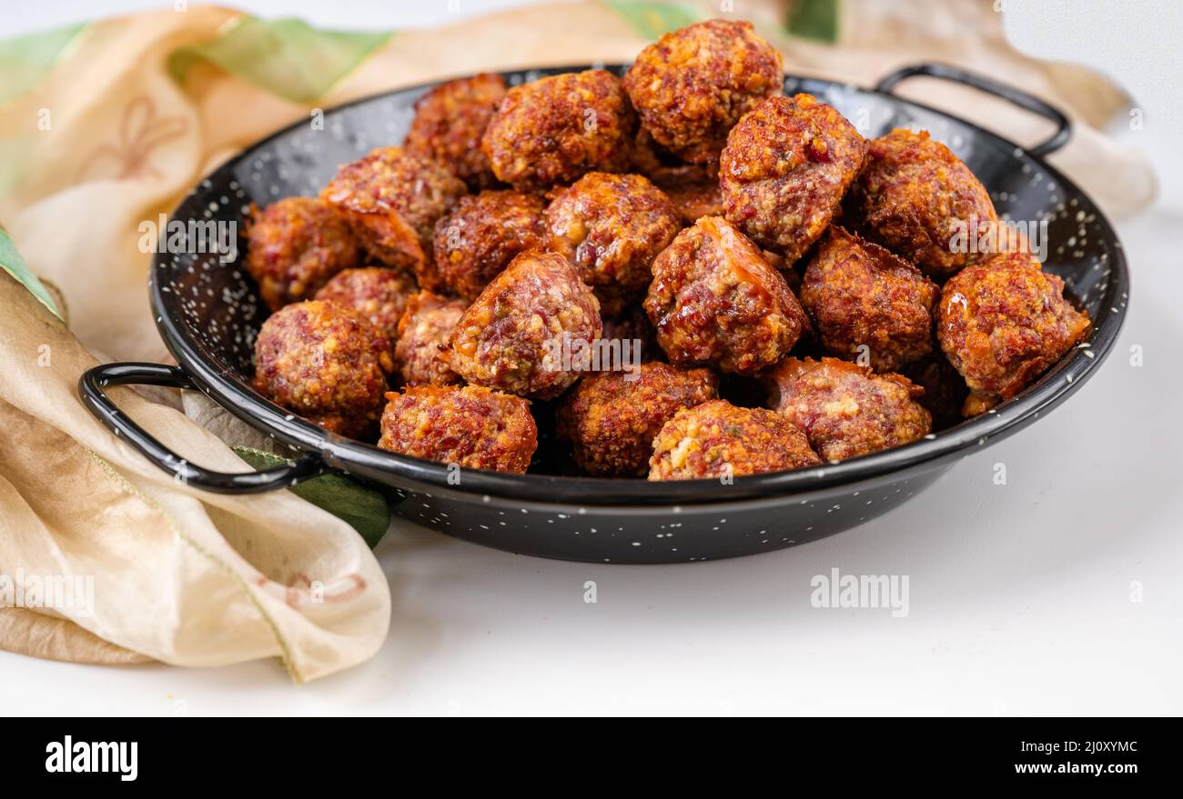 Heap of baked meat ball on rustic black pan, scarf on white background, closeup. Stock Photo