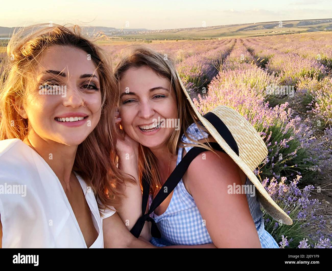 Two happy women female friends taking selfie while standing in lavender field on summer sunny day Stock Photo