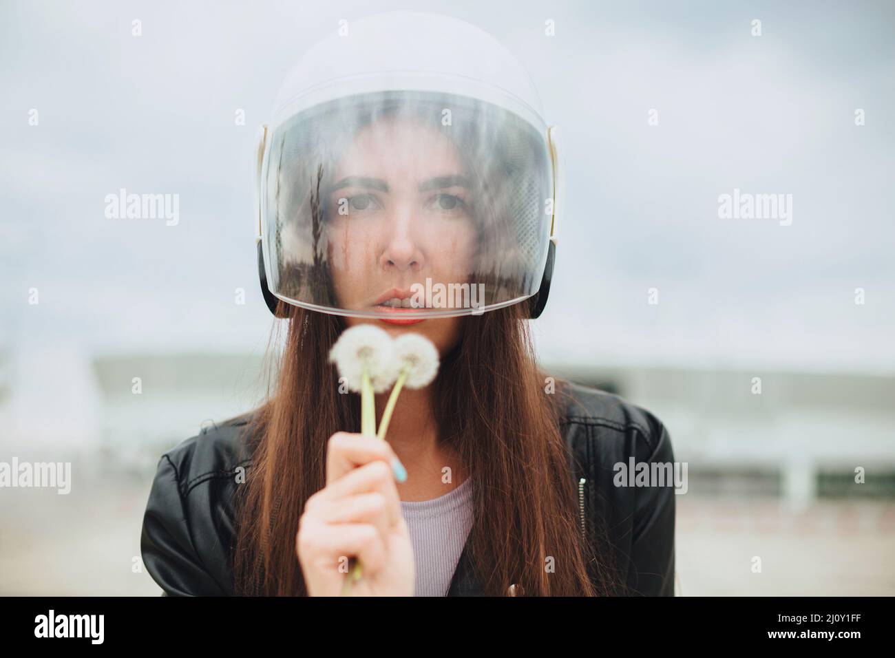 Young woman biker in bike safety helmet and leather outfit with dandelions flowers in hands Stock Photo