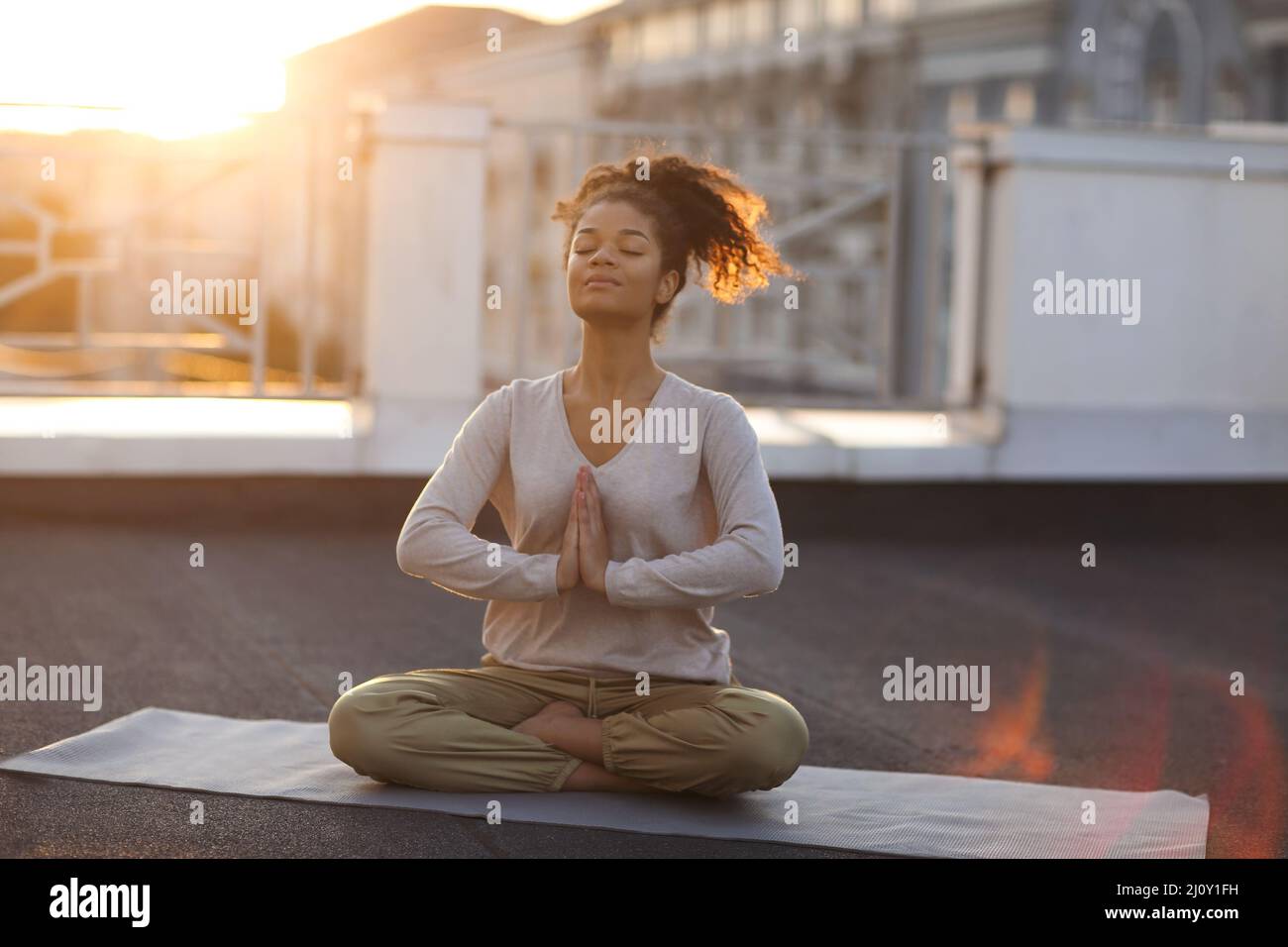 Woman sitting in lotus pose on mat and practicing yoga, female meditating indoors Stock Photo