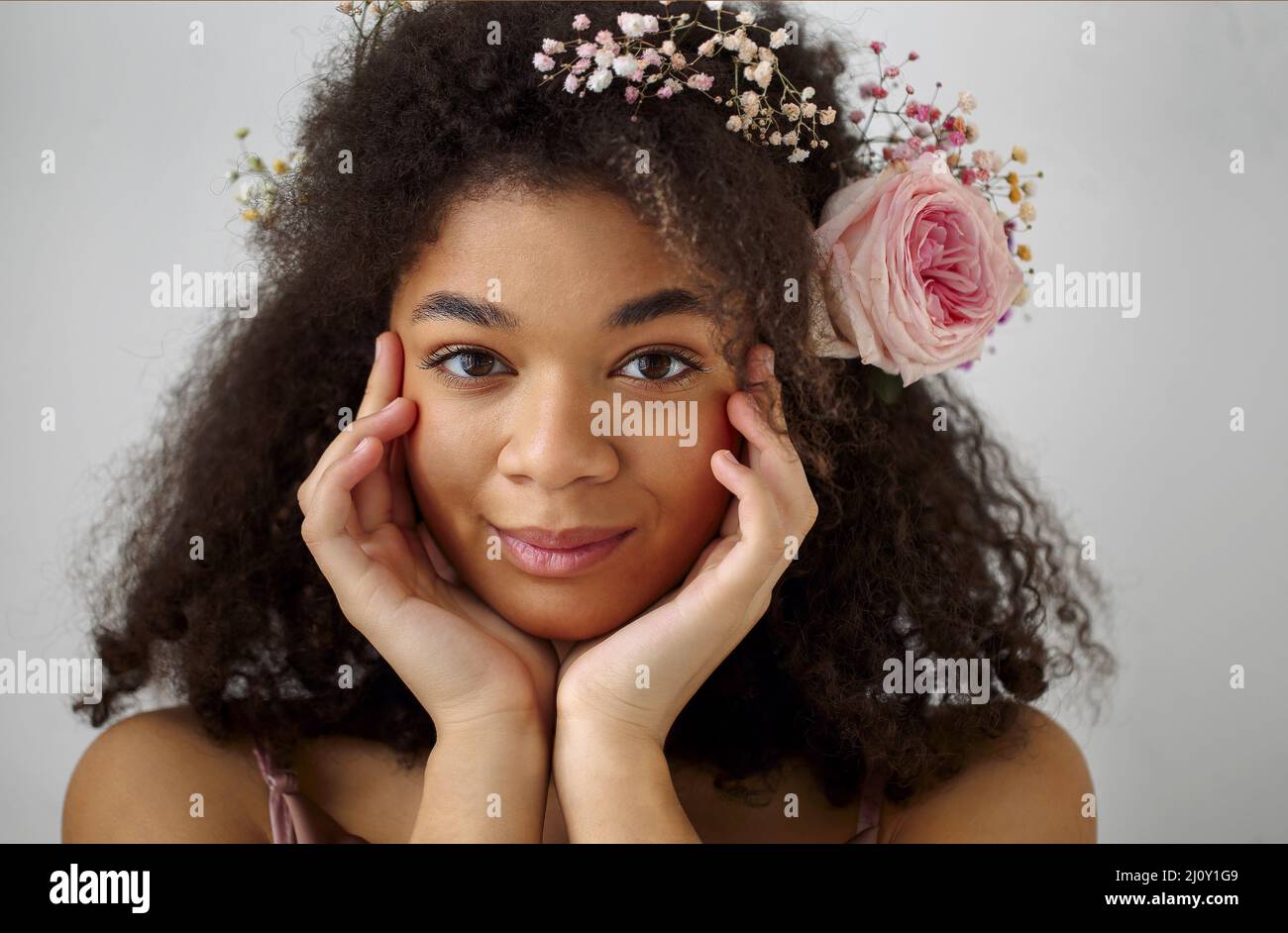 Spring portrait of gorgeous african american young woman with fresh pink rose flower in curly hair Stock Photo
