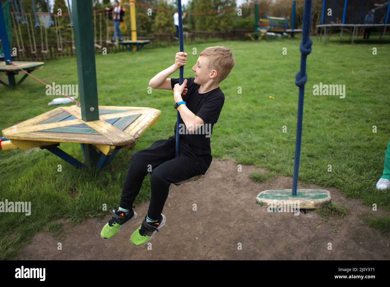 the boy goes through an obstacle course is engaged in active sports sits on a suspended swing Stock Photo