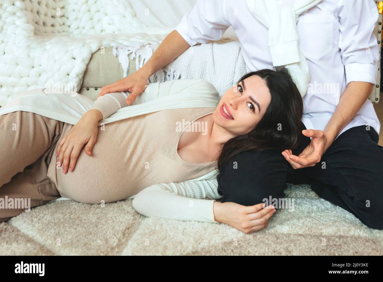 Young family couple waiting for baby. View from above of loving husband hugging pregnant wife while relaxing together at home, m Stock Photo