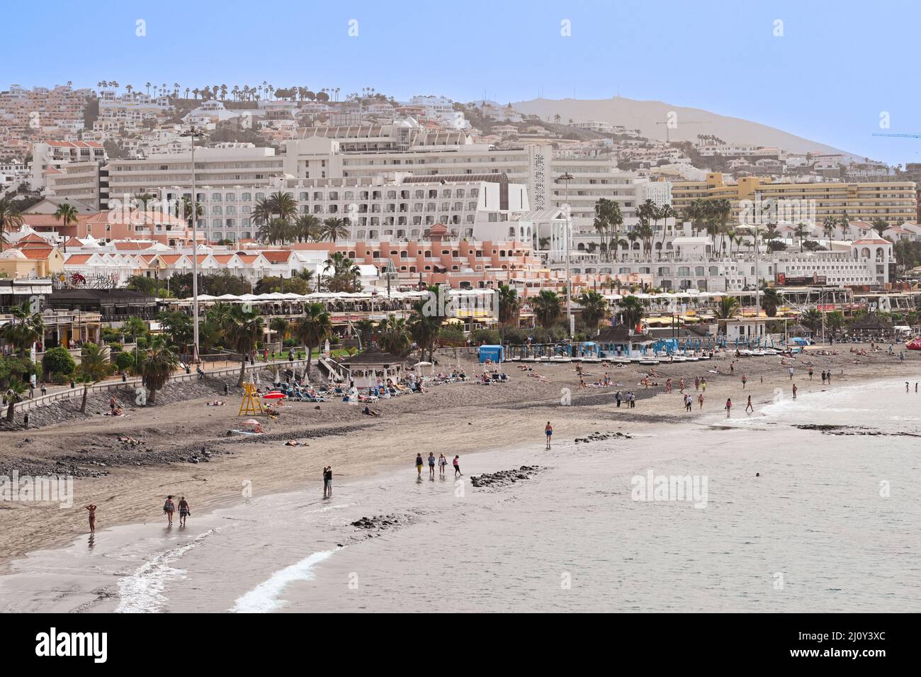 A view of a beach with imported sand mixed in with the natural volcanic sand in Costa Adeje, Tenerife with holiday makers enjoying the sunshine Stock Photo