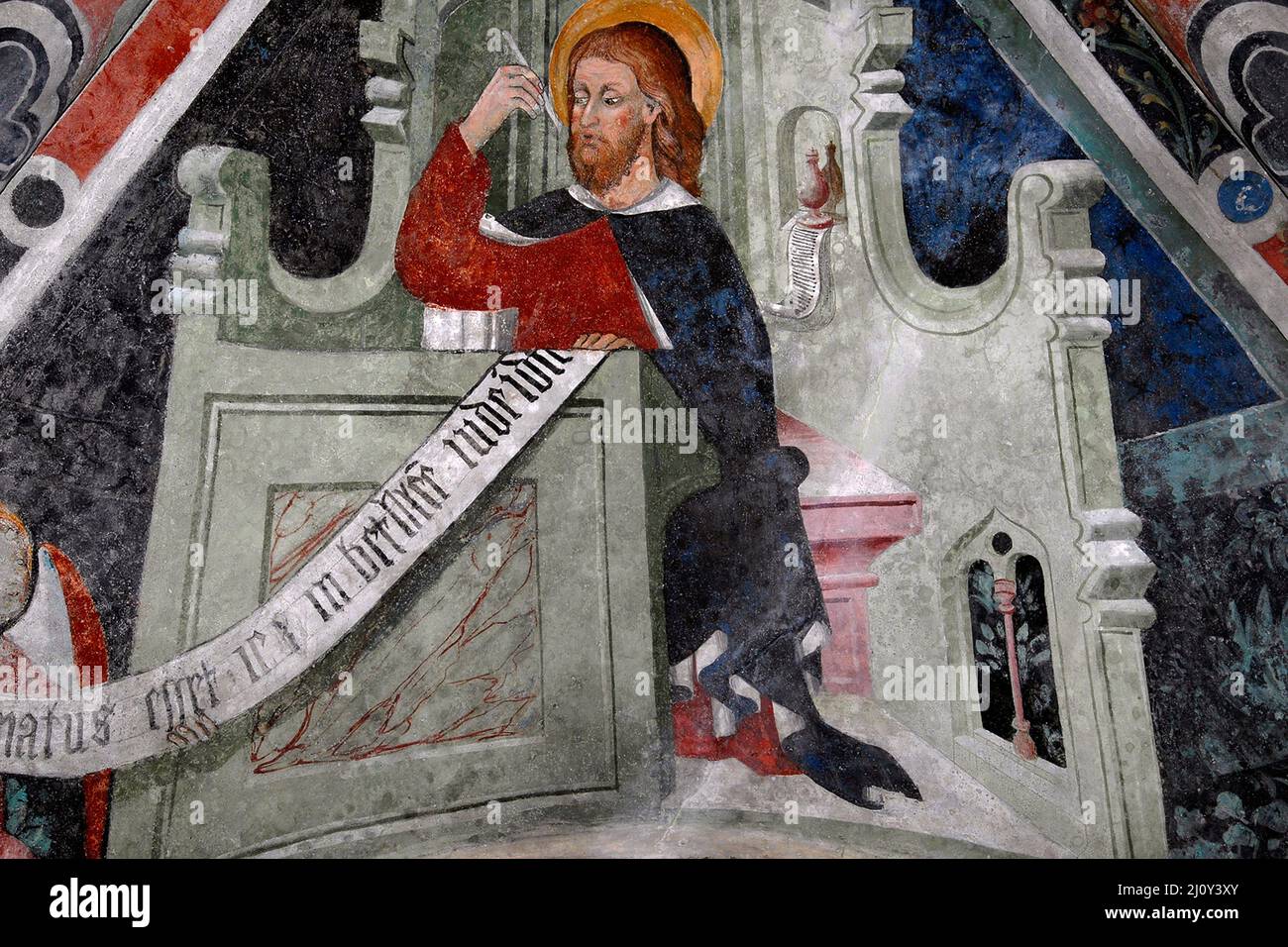 Red-haired Saint Matthew the Evangelist sits at a desk writing his Gospel in 1400s Piedmontese Late Gothic fresco cycle.  On ceiling vault in the church of the former Franciscan convent at Susa, Piedmont, Italy. Stock Photo