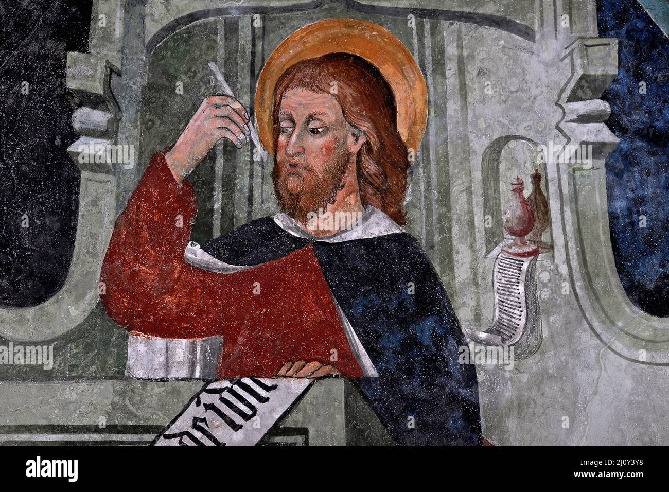 Red-haired Saint Matthew the Evangelist sits at a desk writing his Gospel in 1400s Piedmontese Late Gothic fresco cycle.  On ceiling vault in the church of the former Franciscan convent at Susa, Piedmont, Italy. Stock Photo