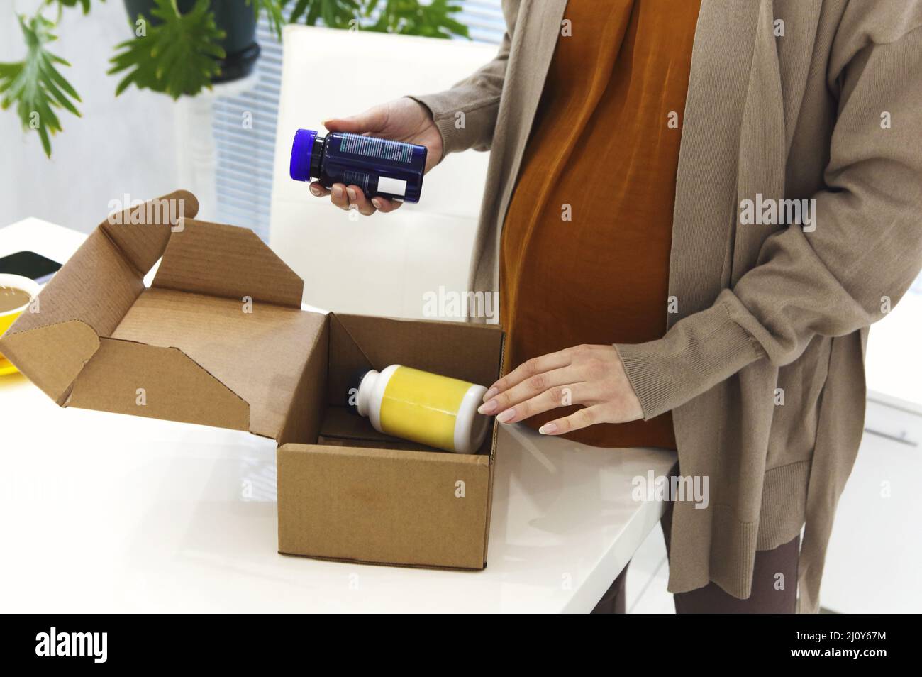 Cropped photo of pregnant woman at home opening cardboard delivery box with prenatal vitamins Stock Photo