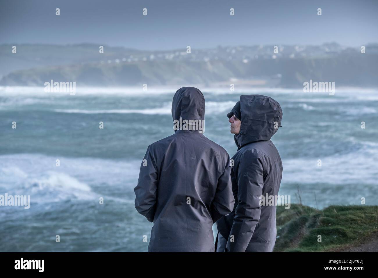 People wearing waterproof jackerts with hoods up in storm force wind brought by Storm Eunice as it arrives in Newquay in Cornwall. Stock Photo