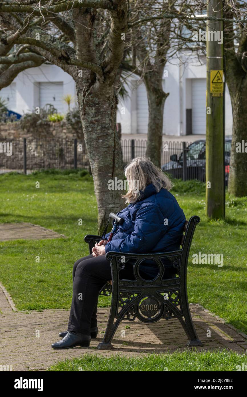 A mature woman sitting alone on a park bench in Trenance Gardens in Newquay in Cornwall in the UK. Stock Photo
