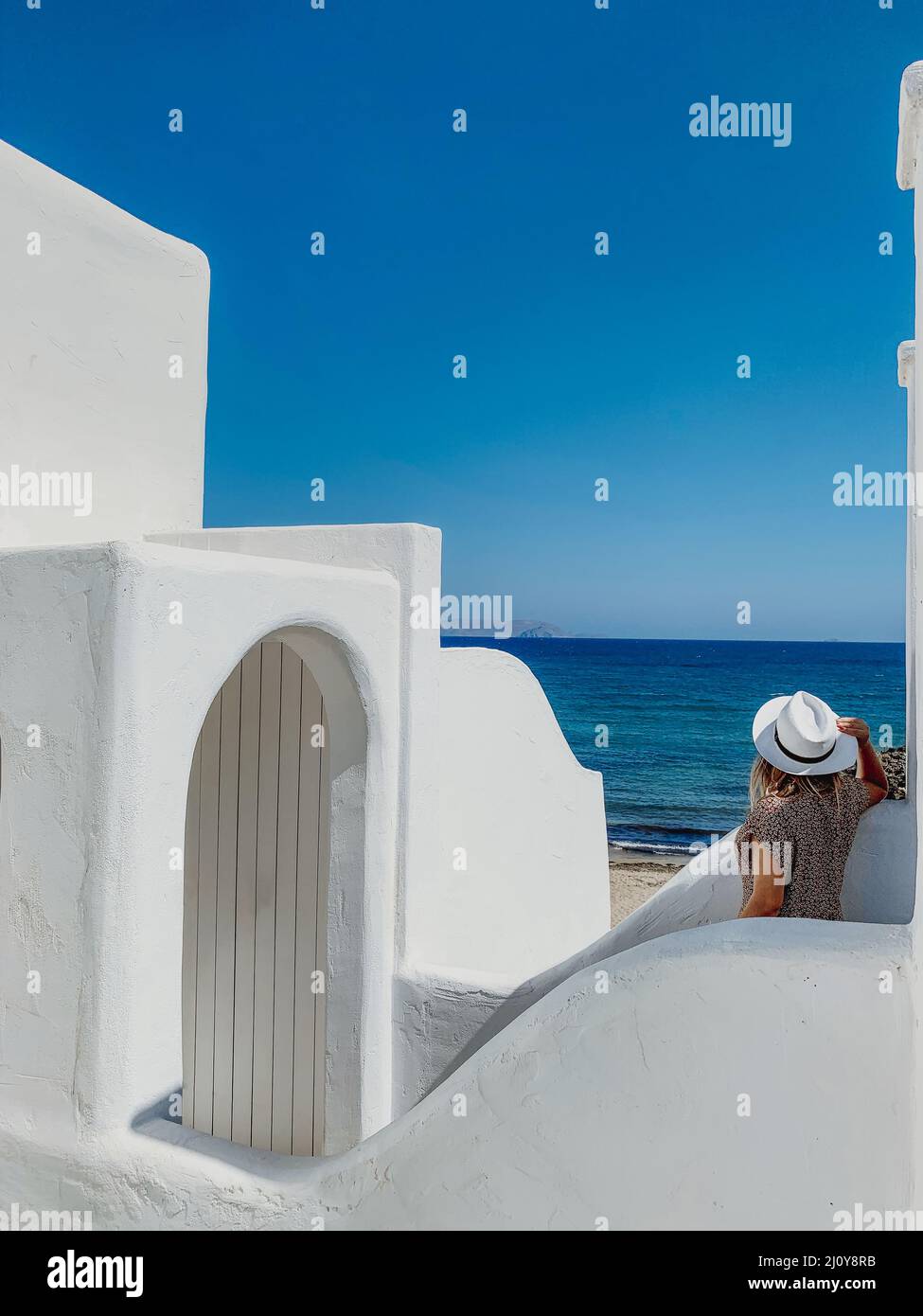 Happy blonde in straw hat standing on white terrace of resort hotel Stock Photo
