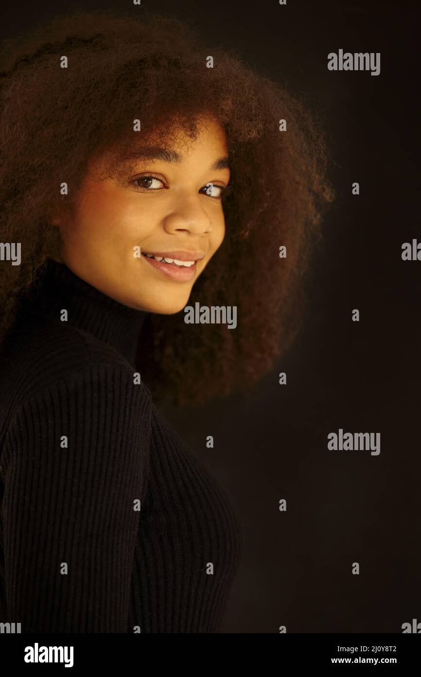 African beauty. Smiling young african-american woman in black clothes isolated on dark background Stock Photo