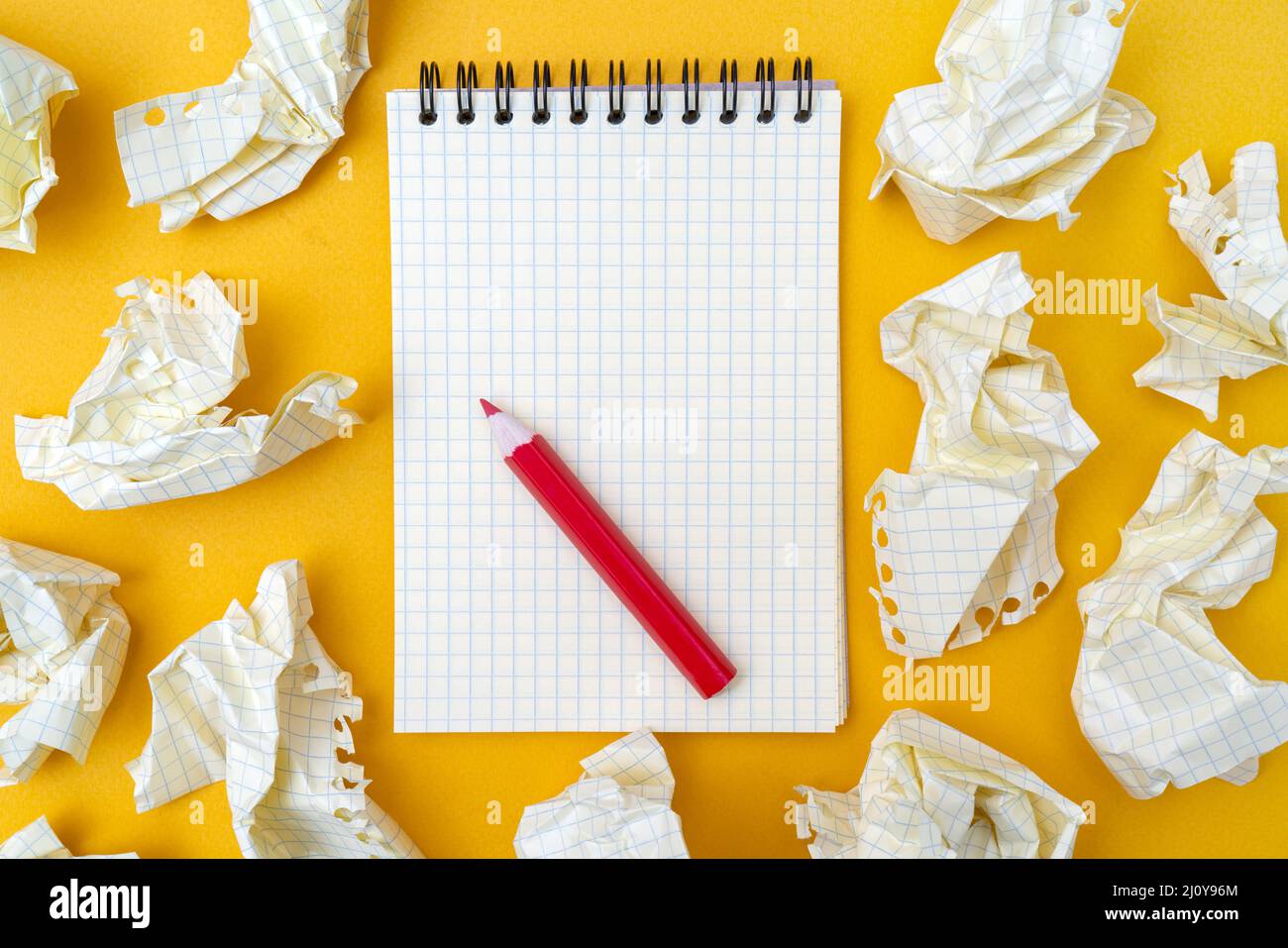 Red pencil and notebook on a yellow background. Crumpled sheets of paper. Stock Photo