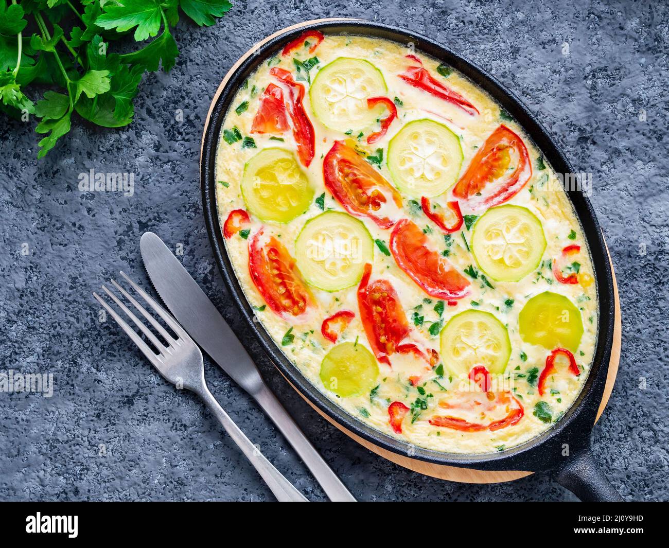 Pan with traditional Italian Frittata on dark gray stone table, forks