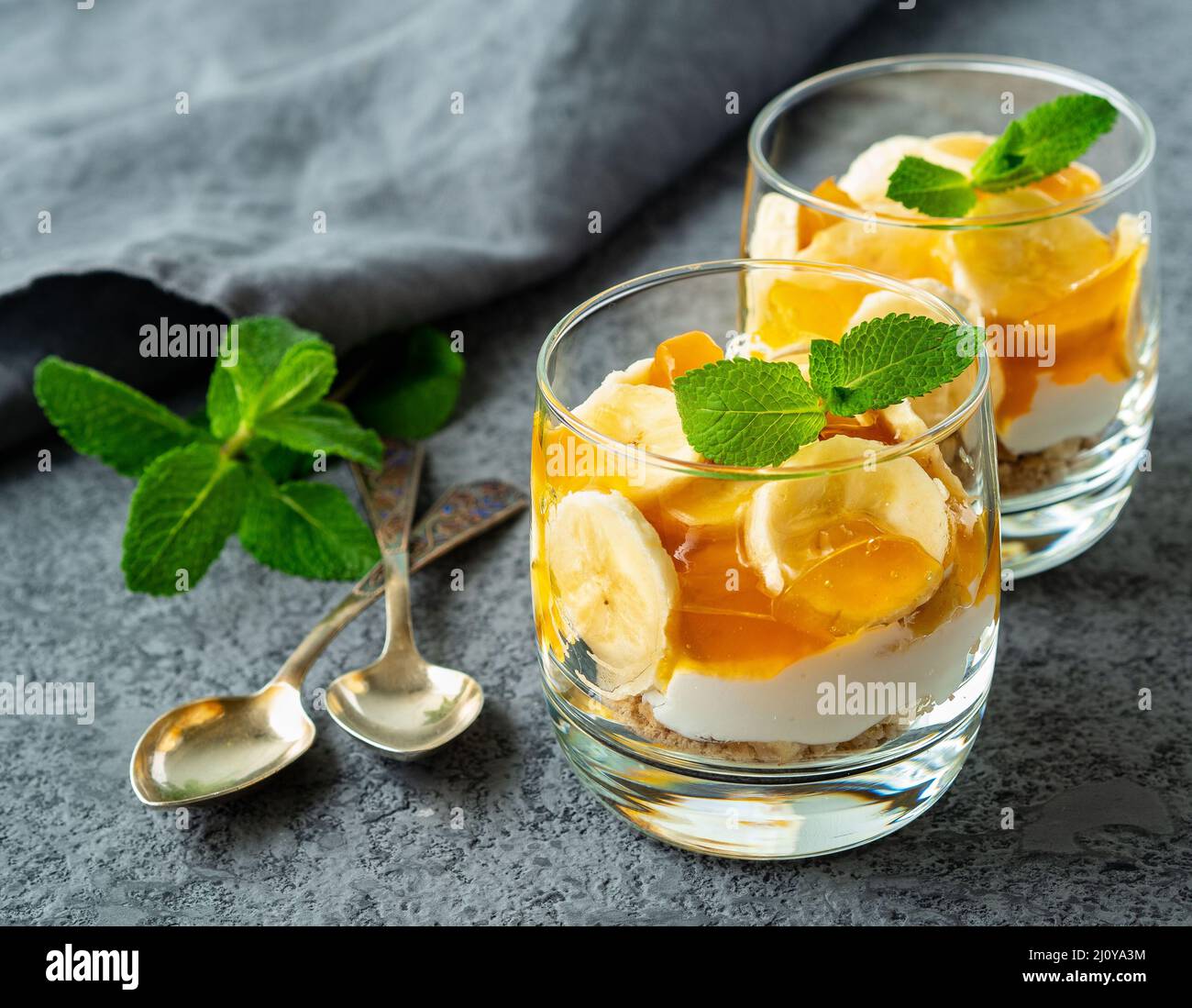 Healthy layered dessert with yogurt, banana, mango jam, cookie in glass