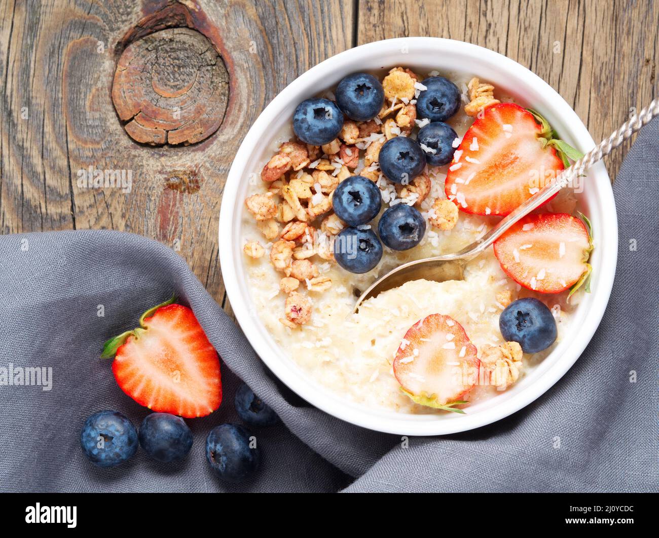 Oatmeal porridge with fresh strawberry, blueberry, granola on old rustic wooden background. Healthy breakfast. Top view. Stock Photo