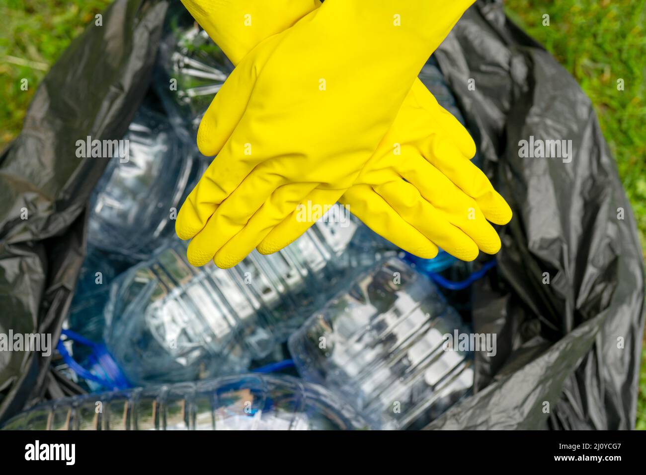 https://c8.alamy.com/comp/2J0YCG7/crossed-hands-in-yellow-gloves-against-a-black-pklastic-bag-with-empty-plastic-bottles-plastic-ban-2J0YCG7.jpg