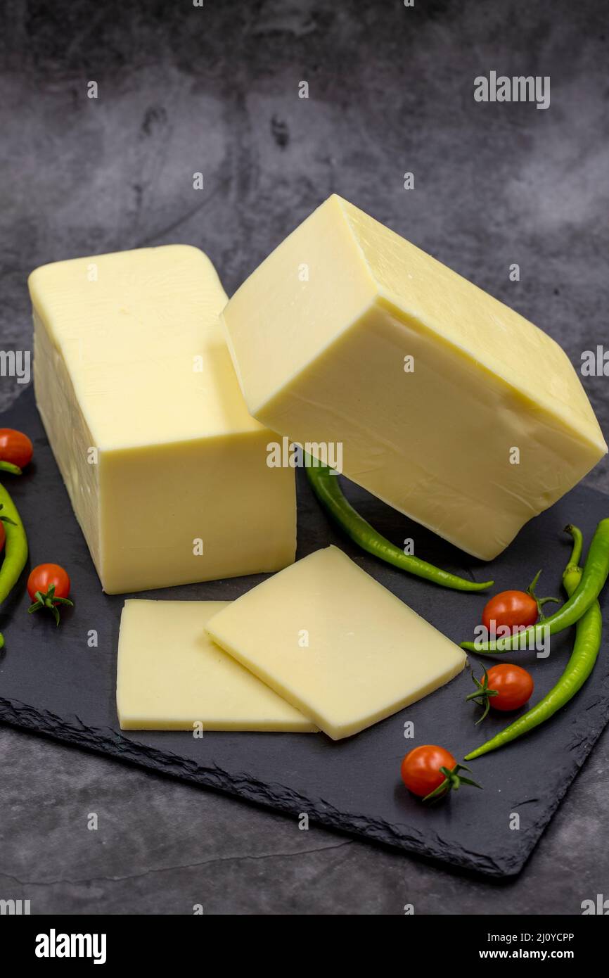 Cheddar cheese or kashkaval cheese on dark background. Cheese slices on the serving board Stock Photo