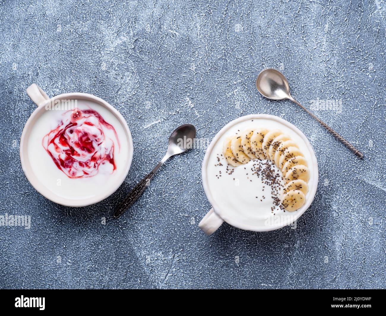 Greek yogurt with jam in white bowl on grey blue concrete stone table, top view, copy space