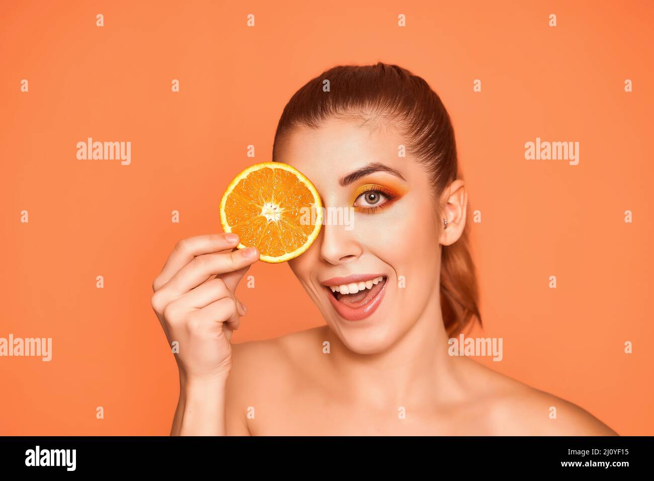 Closeup portrait of beautiful smiling girl , holding half of oranges near face, isolated on orange background. Beauty and health care concept. High quality photo.  Stock Photo