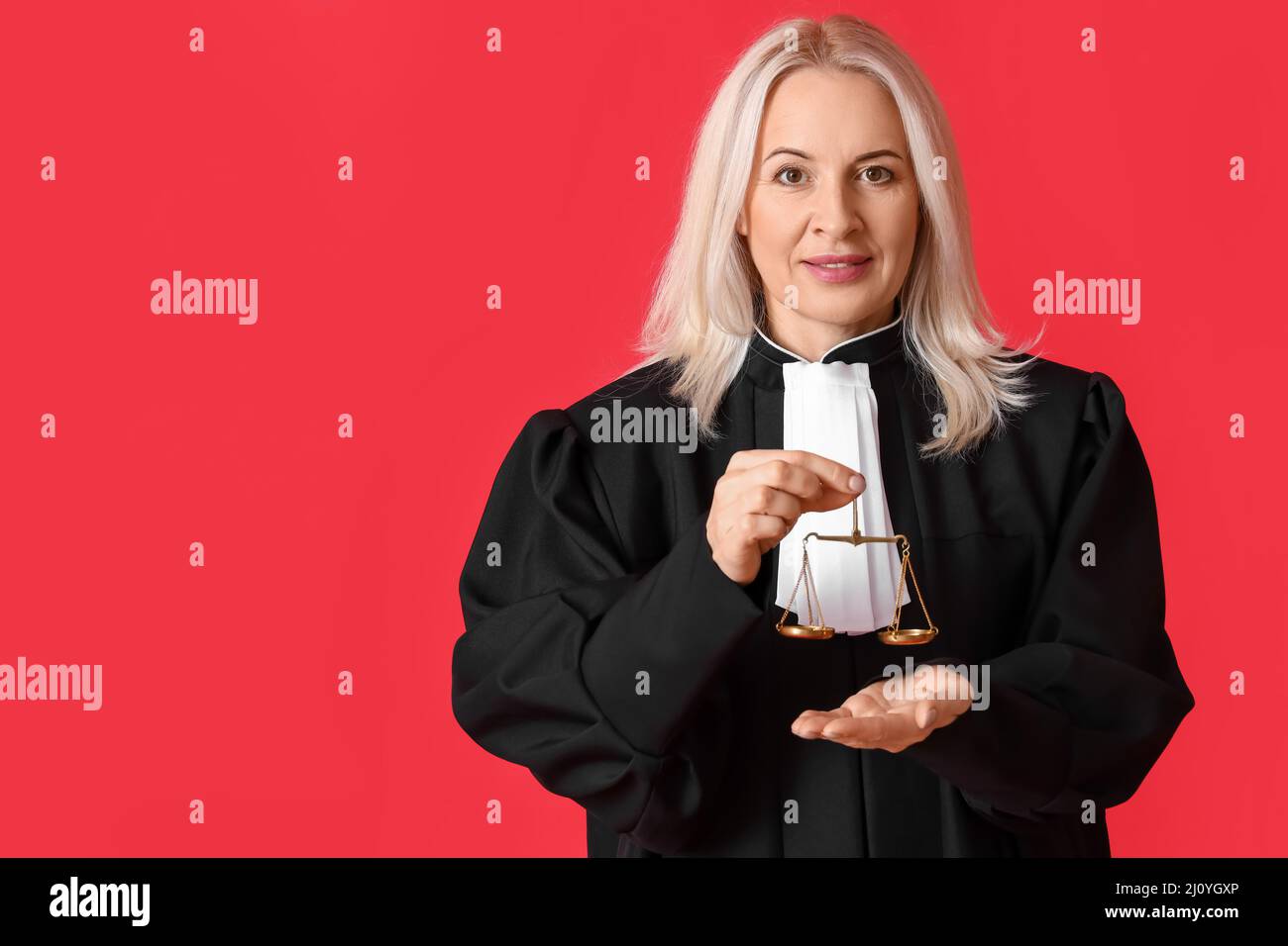 Mature female judge in robe with justice scales on red background Stock ...